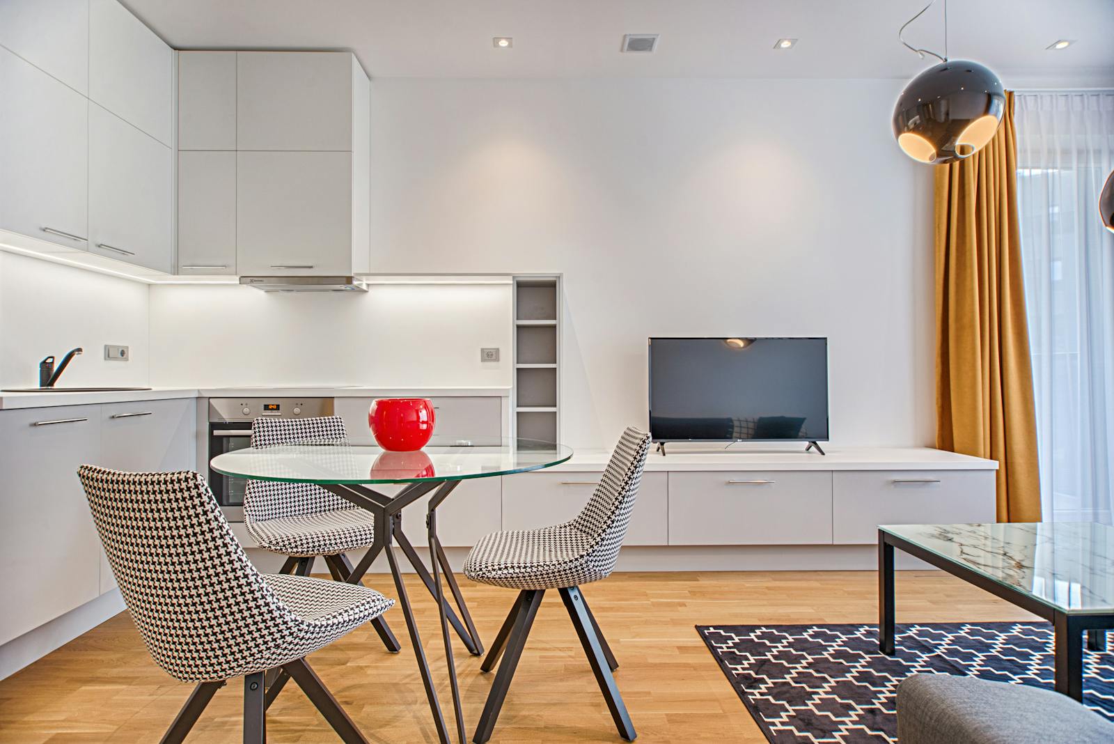 Sleek modern living room with houndstooth chairs, wooden floor, and a glass table.